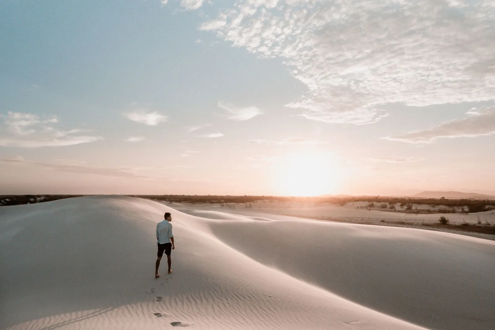Einzelner Mann geht bei Sonnenuntergang über eine Sanddüne, Fußspuren im Sand