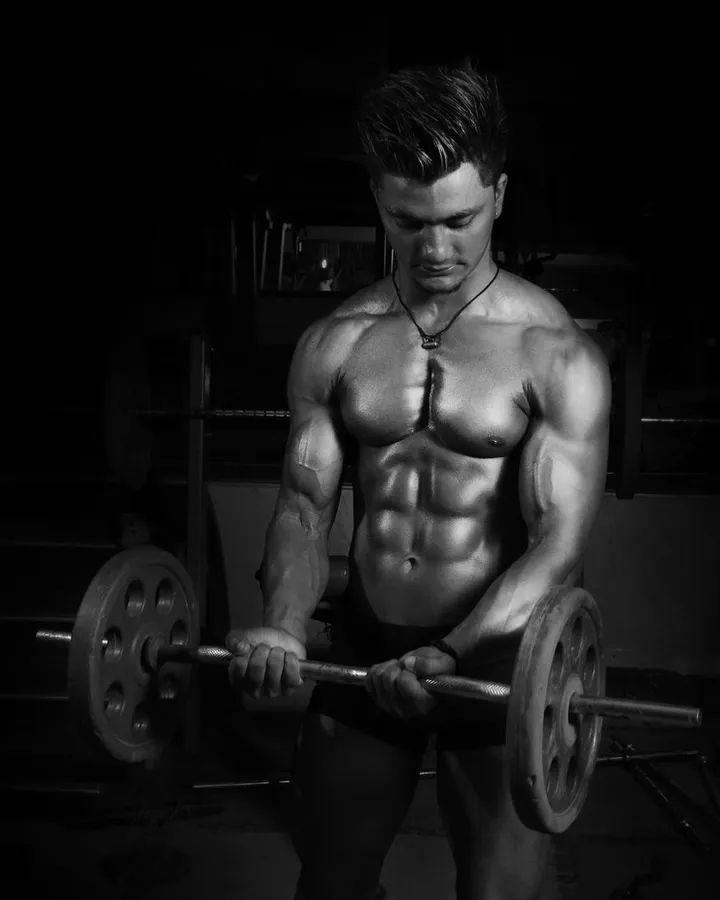 Schwarz-Weiß-Foto: Mann mit nacktem Oberkörper hebt im dunklen Gym eine Langhantel