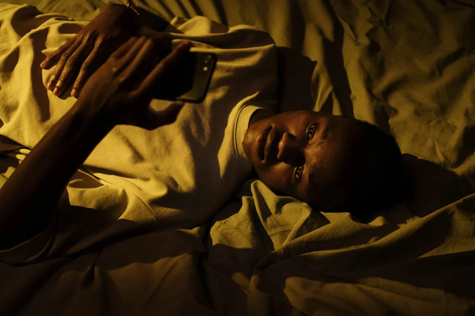Mann liegt nachts im dunklen Schlafzimmer im Bett und schaut auf sein Handy