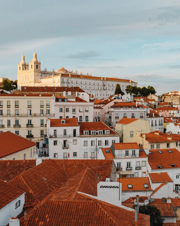 Rote Ziegeldächer der Alfama im warmen Abendlicht, darüber das Kloster São Vicente de Fora